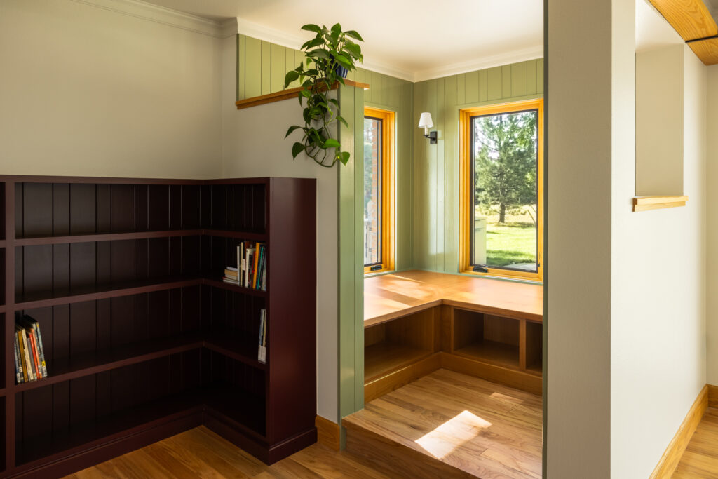 The book nook is a peaceful retreat with built-in shelving crafted from rich wood. A comfortable armchair sits by a large bay window, offering a relaxing space for reading with views of the countryside.